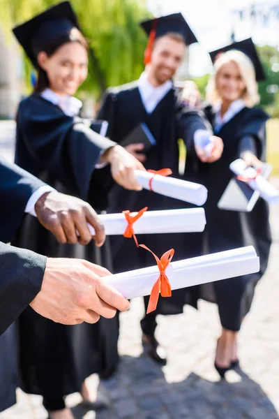 Cropped shot of young graduated students holding rolled diplomas — Stock Photo