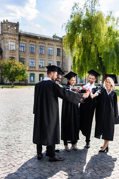 Jóvenes estudiantes graduados felices haciendo gesto de equipo con diplomas laminados - foto de stock