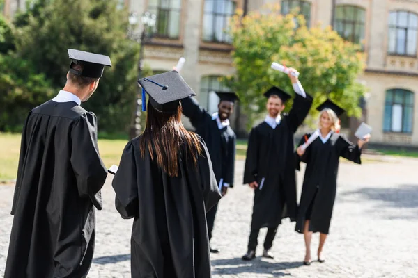 Jóvenes estudiantes graduados que se divierten en el jardín universitario - foto de stock