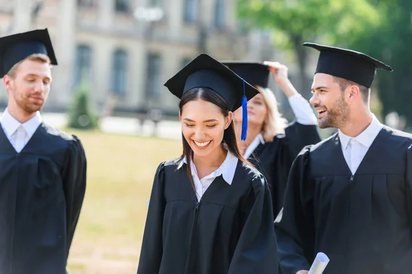 Sorridenti giovani studenti laureati in mantelli sul giardino universitario — Foto stock