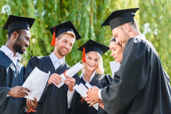 Jóvenes estudiantes graduados felices en capas con diplomas - foto de stock