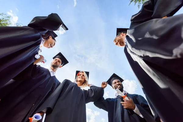 Vista inferior de los jóvenes estudiantes graduados felices delante del cielo azul - foto de stock