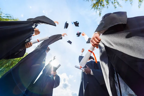 Vue du bas des étudiants diplômés vomissant des chapeaux devant le ciel bleu — Photo de stock