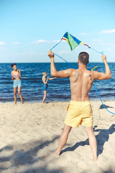 Enfoque selectivo de amigos multiculturales con cometa pasar tiempo en la playa de arena juntos - foto de stock