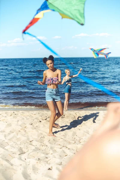 Селективное внимание мультикультурных друзей с воздушными змеями, проводящих время на песчаном пляже вместе — стоковое фото