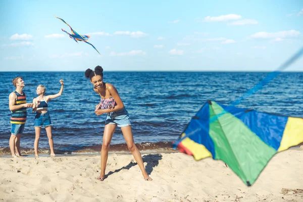 Foco seletivo de amigos multiculturais com pipas passar tempo na praia de areia juntos — Fotografia de Stock