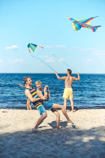 Selective focus of interracial group of friends with kites having fun on sandy beach — Stock Photo