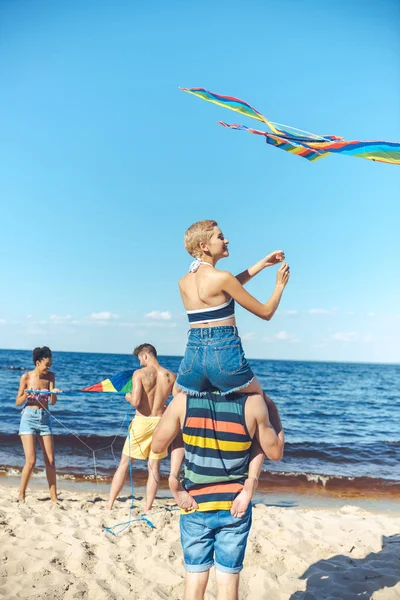 Selective focus of interracial group of friends with kites having fun on sandy beach — Stock Photo