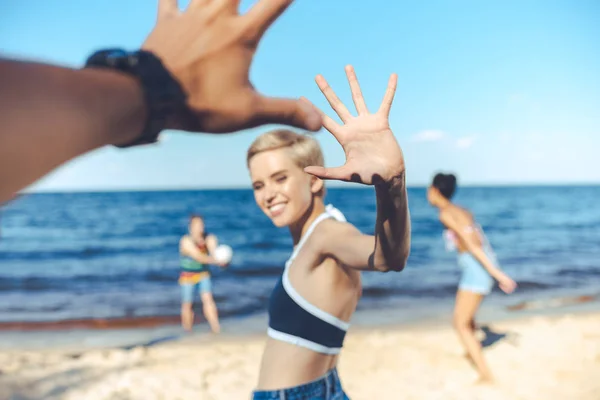 Partial view of smiling woman giving high five to man while multicultural friends playing volleyball on beach — Stock Photo