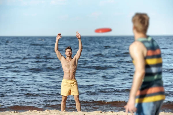 Messa a fuoco selettiva di giovani uomini che giocano con disco volante sulla spiaggia di sabbia — Foto stock