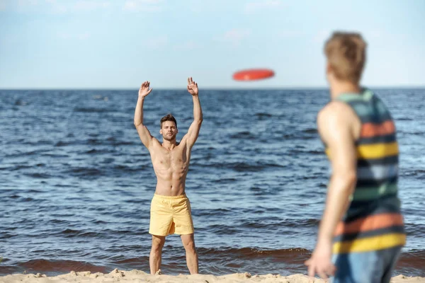 Selektiver Fokus junger Männer, die mit fliegender Scheibe am Sandstrand spielen — Stockfoto