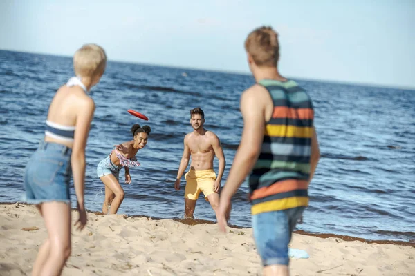 Вибірковий фокус багаторасових друзів, які грають з літаючим диском разом на пляжі — стокове фото
