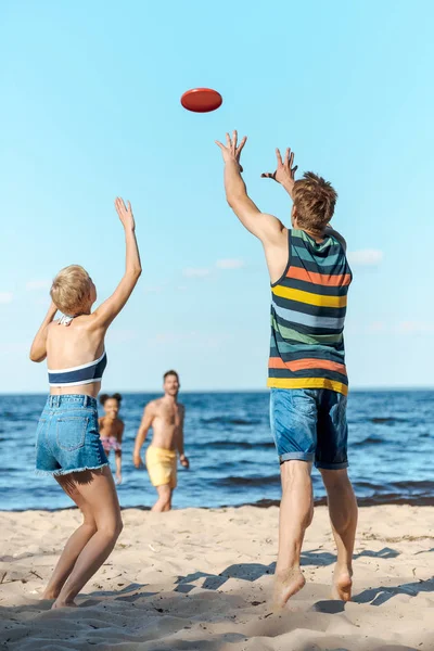 Foco seletivo de amigos multirraciais brincando com disco voador juntos na praia — Fotografia de Stock