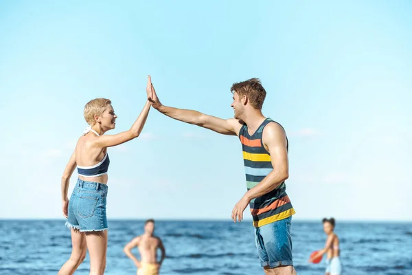 Foco seletivo de amigos multirraciais brincando com disco voador juntos na praia — Fotografia de Stock