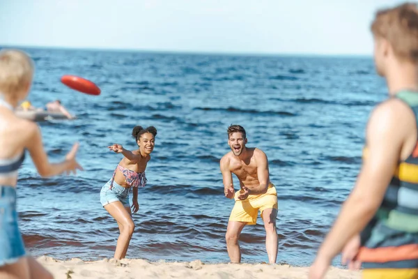 Foco seletivo de amigos multirraciais brincando com disco voador juntos na praia — Fotografia de Stock