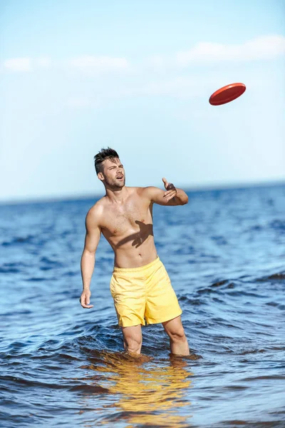 Young man throwing flying disc while standing in sea on summer day — Stock Photo