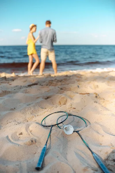 Foco seletivo de equipamentos de badminton e casal na praia de areia — Fotografia de Stock