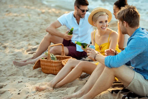 Interracial sonriendo jóvenes amigos con cerveza descansando en la playa de arena juntos en el día de verano - foto de stock