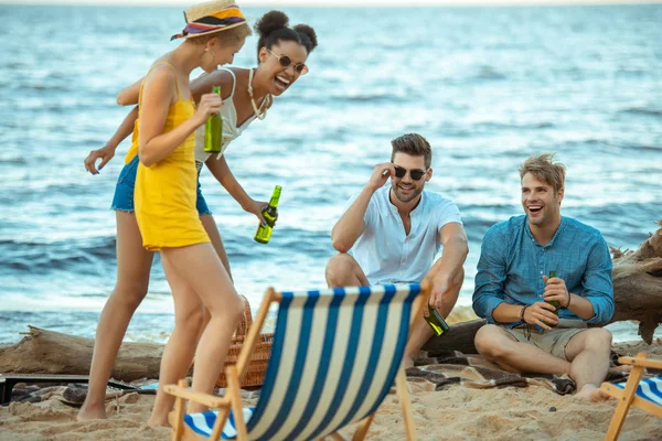 Enfoque selectivo de amigos jóvenes multiculturales con botellas de vidrio de cerveza pasar tiempo juntos en la playa de arena - foto de stock