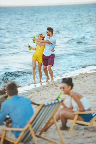 Enfoque selectivo de amigos jóvenes multiculturales con cerveza pasar tiempo juntos en la playa de arena - foto de stock