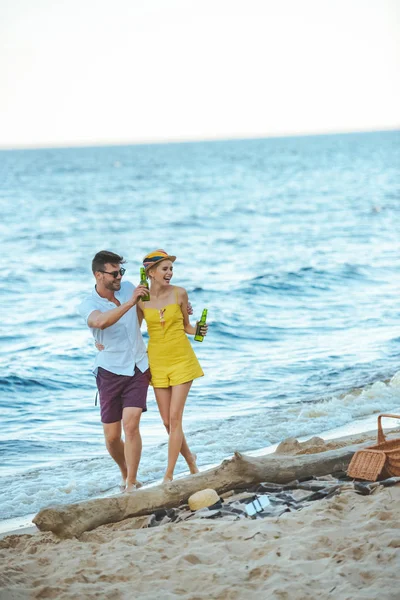 Allegra coppia con birra in bottiglie di vetro passeggiando sulla spiaggia — Foto stock