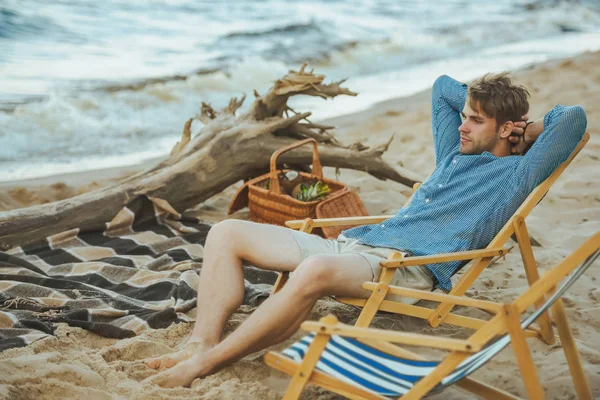 Вид сбоку молодого человека, отдыхающего в пляжном шезлонге на песчаном пляже — стоковое фото
