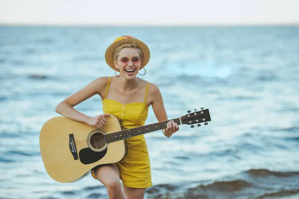 Portrait of happy young woman playing guitar with sea on background — Stock Photo