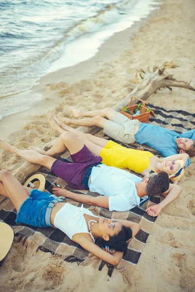 Jovens multirraciais deitado em cobertor enquanto passa o tempo na praia arenosa — Fotografia de Stock