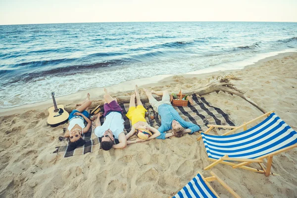 Giovani multietnici sdraiati su una coperta mentre trascorrono del tempo sulla spiaggia sabbiosa — Foto stock