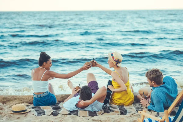 Amigos multiculturales con cocteles de coco y guitarra acústica descansando en la playa de arena - foto de stock