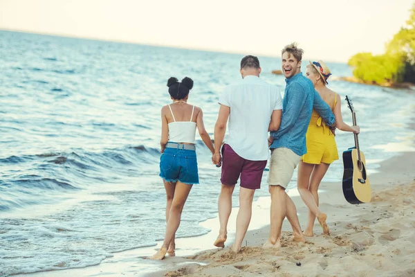 Multiethnische Gruppe von Freunden mit Akustikgitarre, die gemeinsam am Meer spazieren gehen — Stockfoto