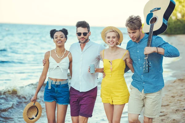 Multiethnic group of friends with acoustic guitar walking together by sea — Stock Photo