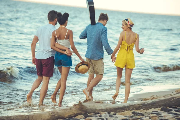 Grupo multiétnico de amigos con guitarra acústica caminando juntos por el mar - foto de stock