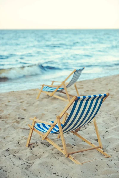 Selective focus of wooden beach chairs on sandy beach with sea on background — Stock Photo