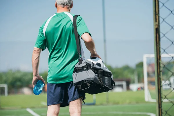 Back view of old man with sportive water bottle and bag on soccer field — Stock Photo