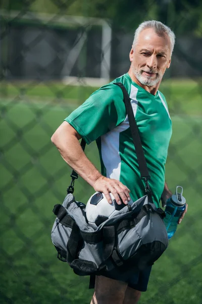 Seitenansicht eines alten Mannes mit sportlicher Wasserflasche und Tasche auf dem Fußballplatz — Stockfoto