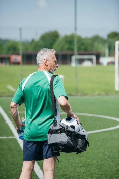 Vista trasera del anciano con botella de agua deportiva y bolsa en el campo de fútbol — Stock Photo