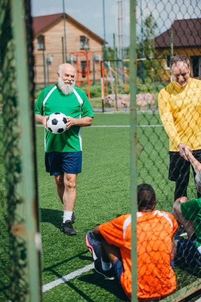 Jogadores de futebol idosos inter-raciais apertando as mãos após o jogo no campo verde — Fotografia de Stock