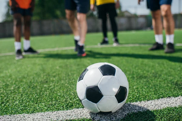 Enfoque selectivo de la pelota de fútbol y los hombres mayores multiculturales en el campo de fútbol verde - foto de stock