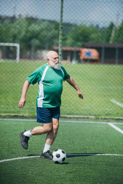 Elderly bearded man playing football on field on summer day — Stock Photo