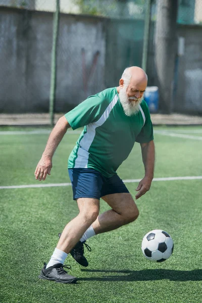 Anziano barbuto giocare a calcio sul campo nella giornata estiva — Foto stock