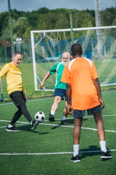 Многорасовые старики вместе играют в футбол на зеленом поле — стоковое фото
