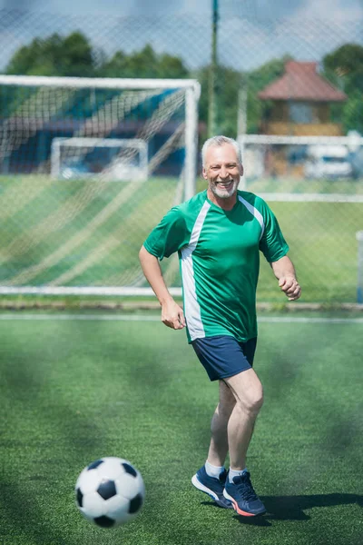 Cheerful old man playing football on field on summer day — Stock Photo