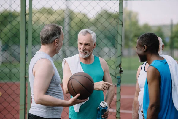 Grupo de viejos deportistas multirraciales con pelota de baloncesto en el patio de recreo - foto de stock