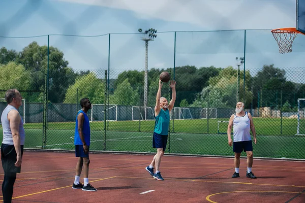 Interracial ancianos deportistas jugando baloncesto juntos en patio de recreo - foto de stock