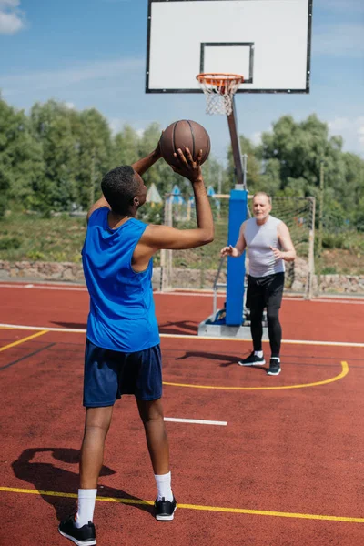 Многорасовые пожилые мужчины играют вместе в баскетбол на детской площадке в летний день — стоковое фото