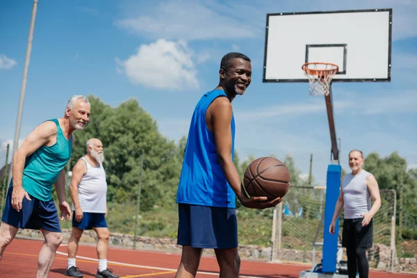 Interracial elderly sportsmen playing basketball together on playground — Stock Photo