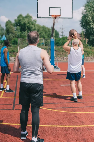 Interracial elderly sportsmen playing basketball together on playground — Stock Photo