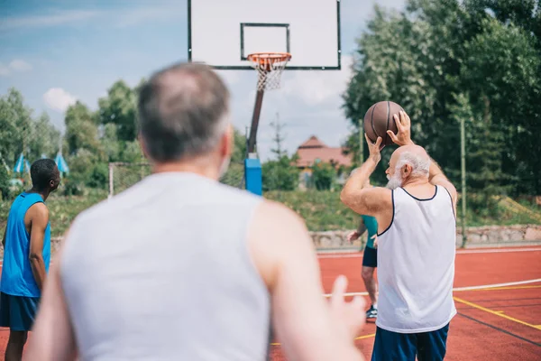 Selective focus of interracial elderly sportsmen playing basketball together on playground — Stock Photo