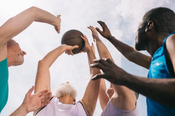Baixo ângulo de visão dos atletas idosos inter-raciais jogando basquete juntos — Fotografia de Stock